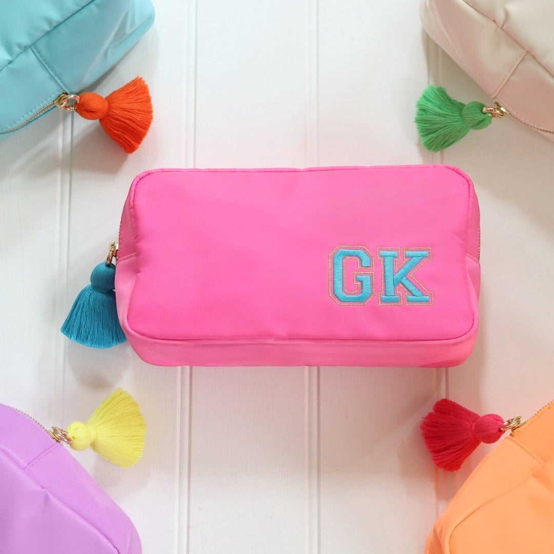 Personalised pink nylon pouch bag with varsity style initials embroidered on in blue with a matching blue tassel zipper pull. Custom travel clutch handbag for cosmetics, toiletries or everyday essential - perfect gift for her.