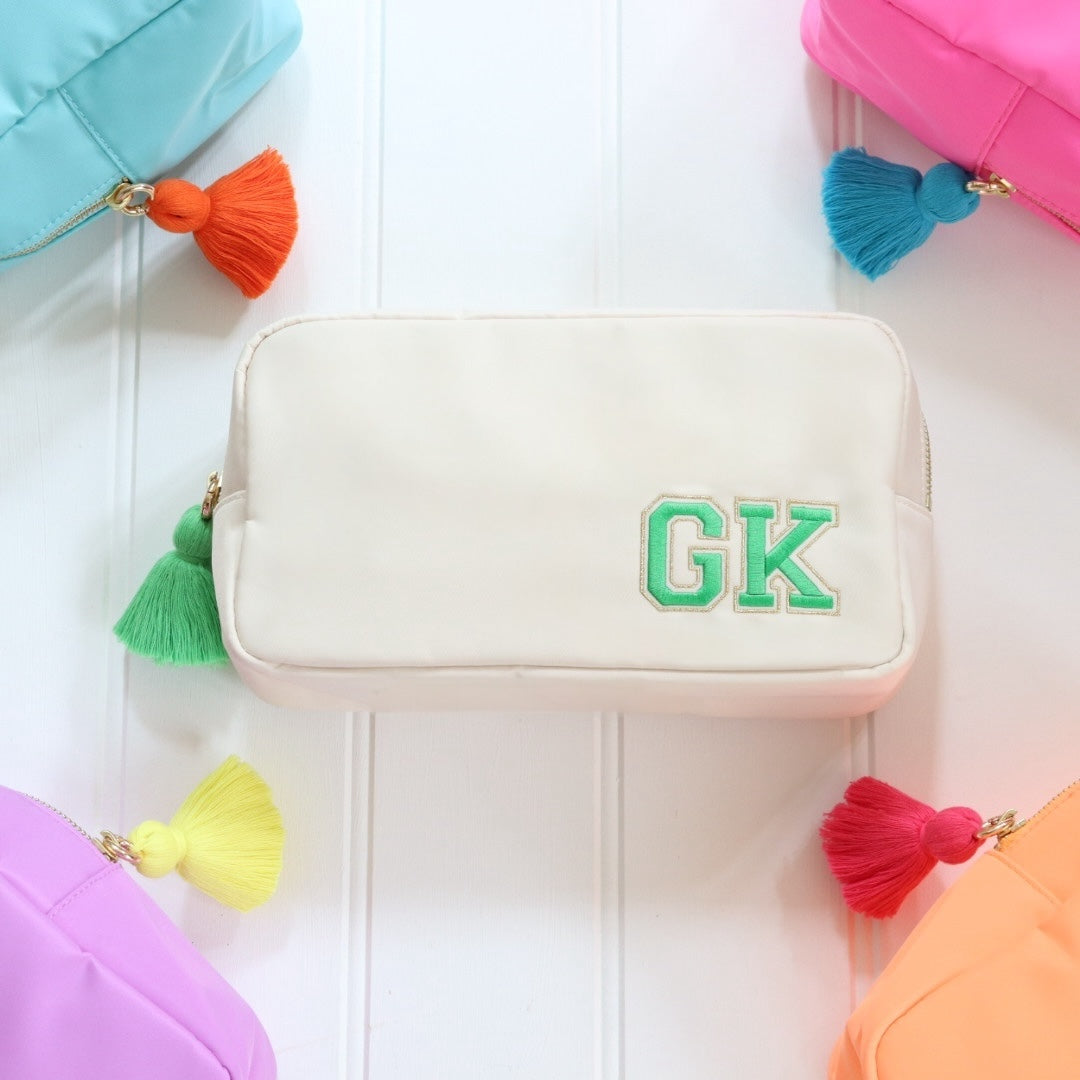 Personalised cream nylon pouch bag with varsity style initials embroidered on in green with a matching green tassel zipper pull. Custom travel clutch handbag for cosmetics, toiletries or everyday essential - perfect gift for her.