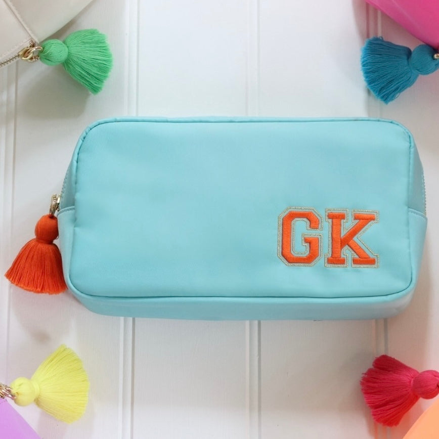 Personalised blue nylon pouch bag with varsity style initials embroidered on in orange with a matching orange tassel zipper pull. Custom travel clutch handbag for cosmetics, toiletries or everyday essential - perfect gift for her.