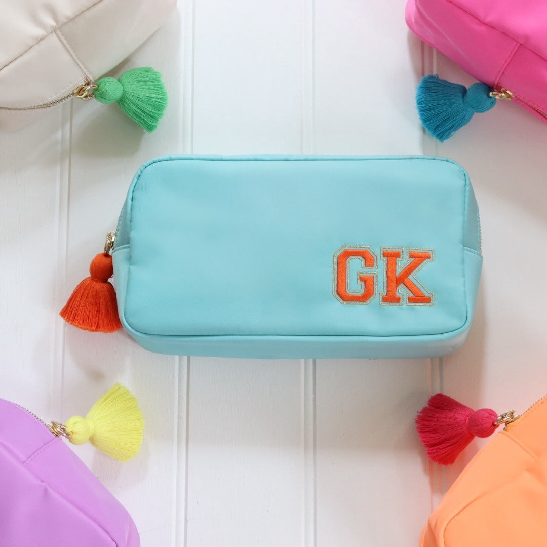 Personalised blue nylon pouch bag with varsity style initials embroidered on in orange with a matching orange tassel zipper pull. Custom travel clutch handbag for cosmetics, toiletries or everyday essential - perfect gift for her