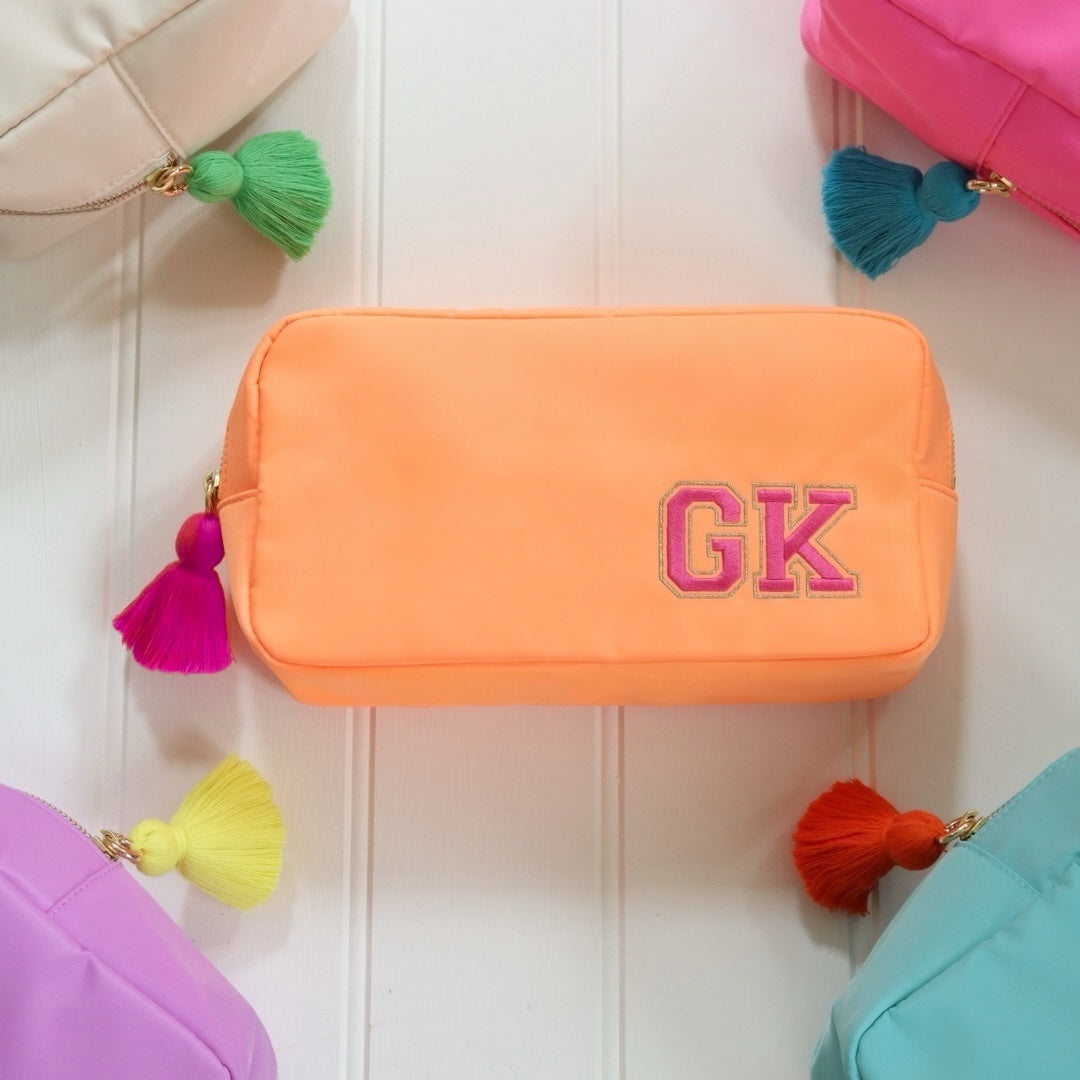 Personalised orange nylon pouch bag with varsity style initials embroidered on in pink with a matching pink tassel zipper pull. Custom travel clutch handbag for cosmetics, toiletries or everyday essential - perfect gift for her.