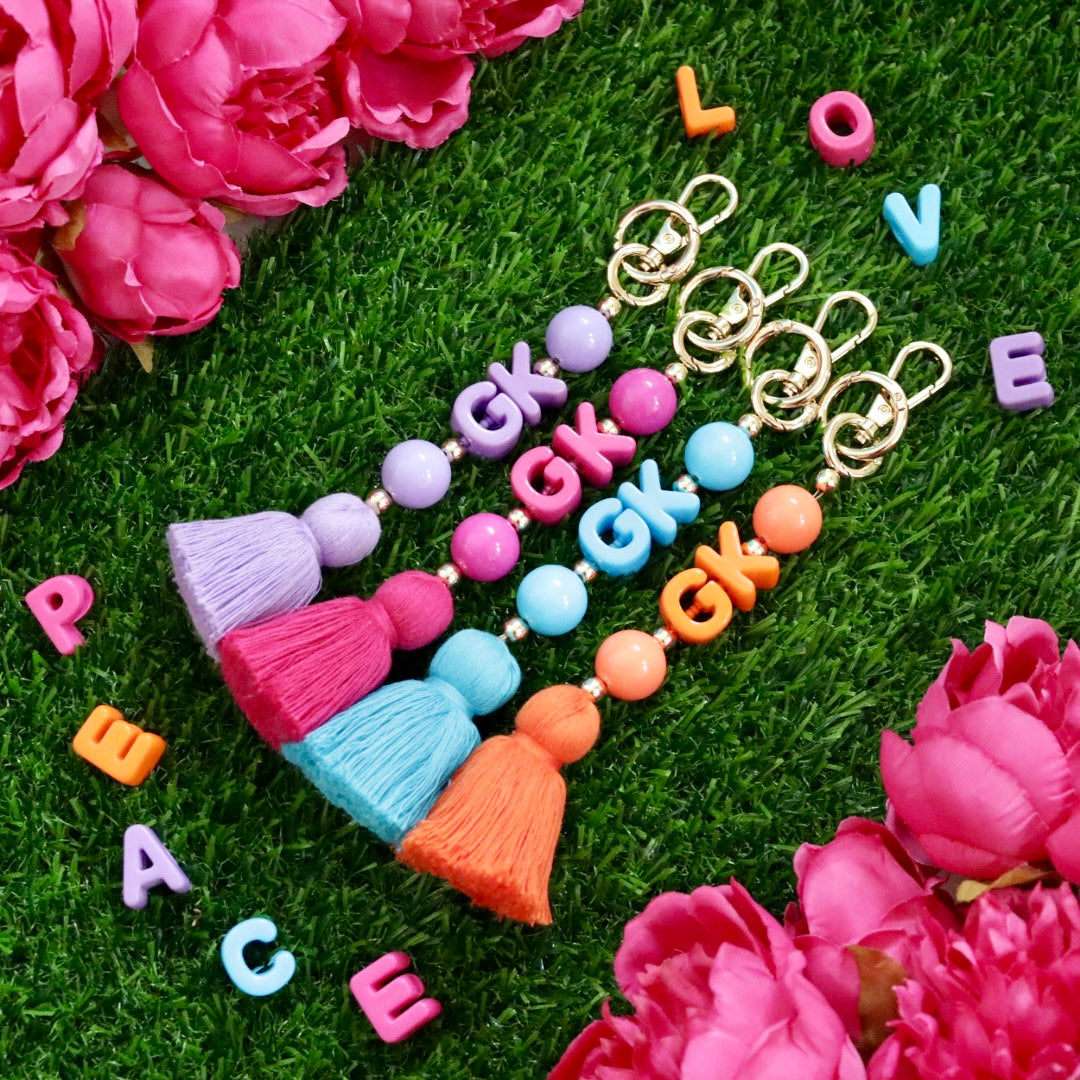Personalised beaded keychain or bag charm in a choice of lilac, fuchsia, blue or orange with gold accents, chunky bead custom initials & matching colour tassel. Perfect gift for her.