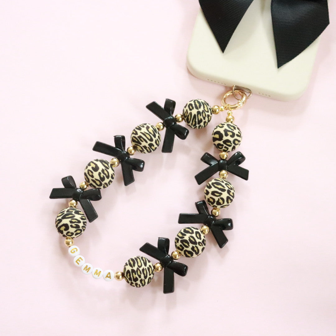 Personalised leopard print & black bow beaded wristlet phone charm with gold accents, featuring optional custom name or initial beads. The perfect gift for girls, women or teens.