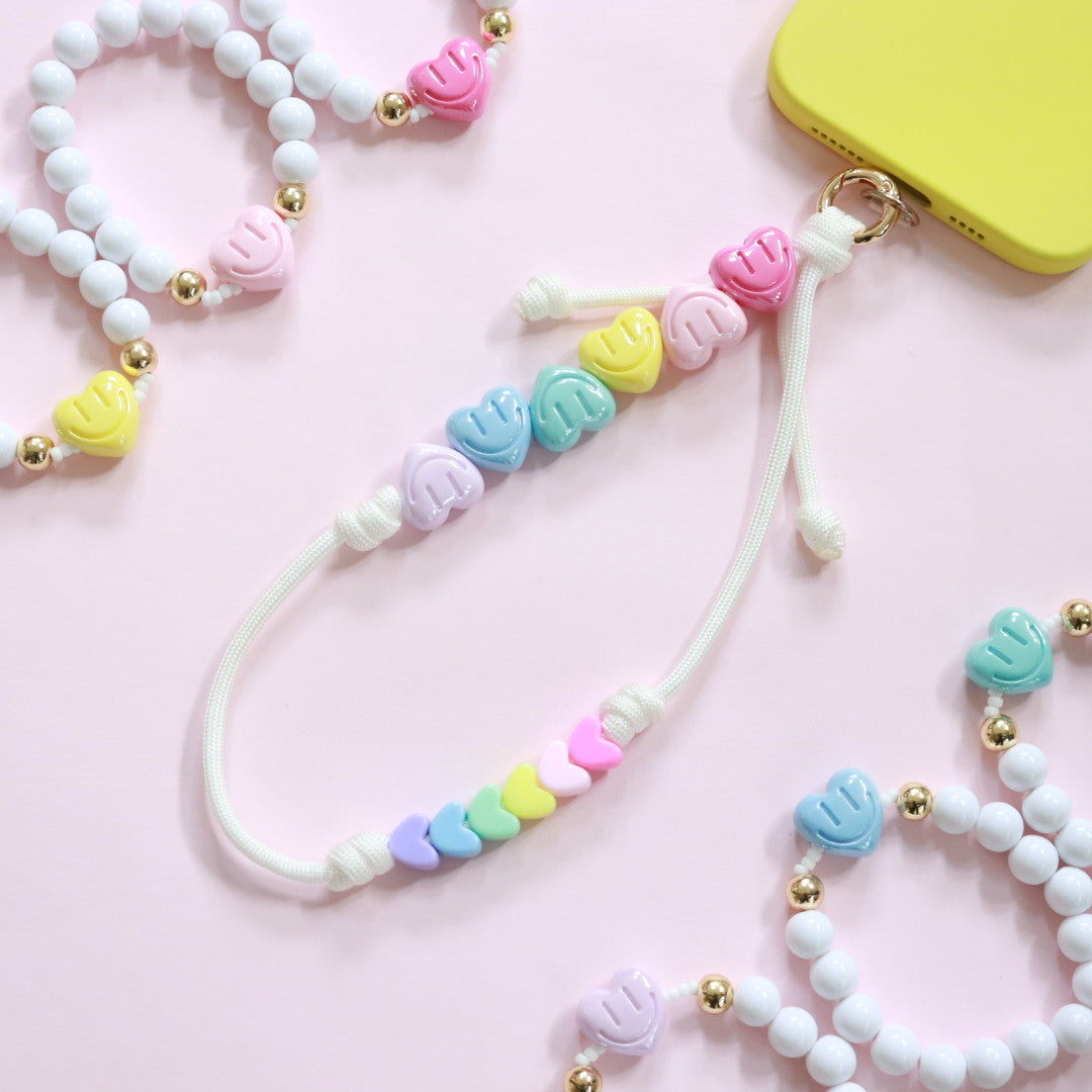 Handmade beaded phone charm featuring smiling face & heart shaped beads strung on to a choice of white or 6 brightly coloured paracords with gold accents. The Perfect gift for girls, women or teens.