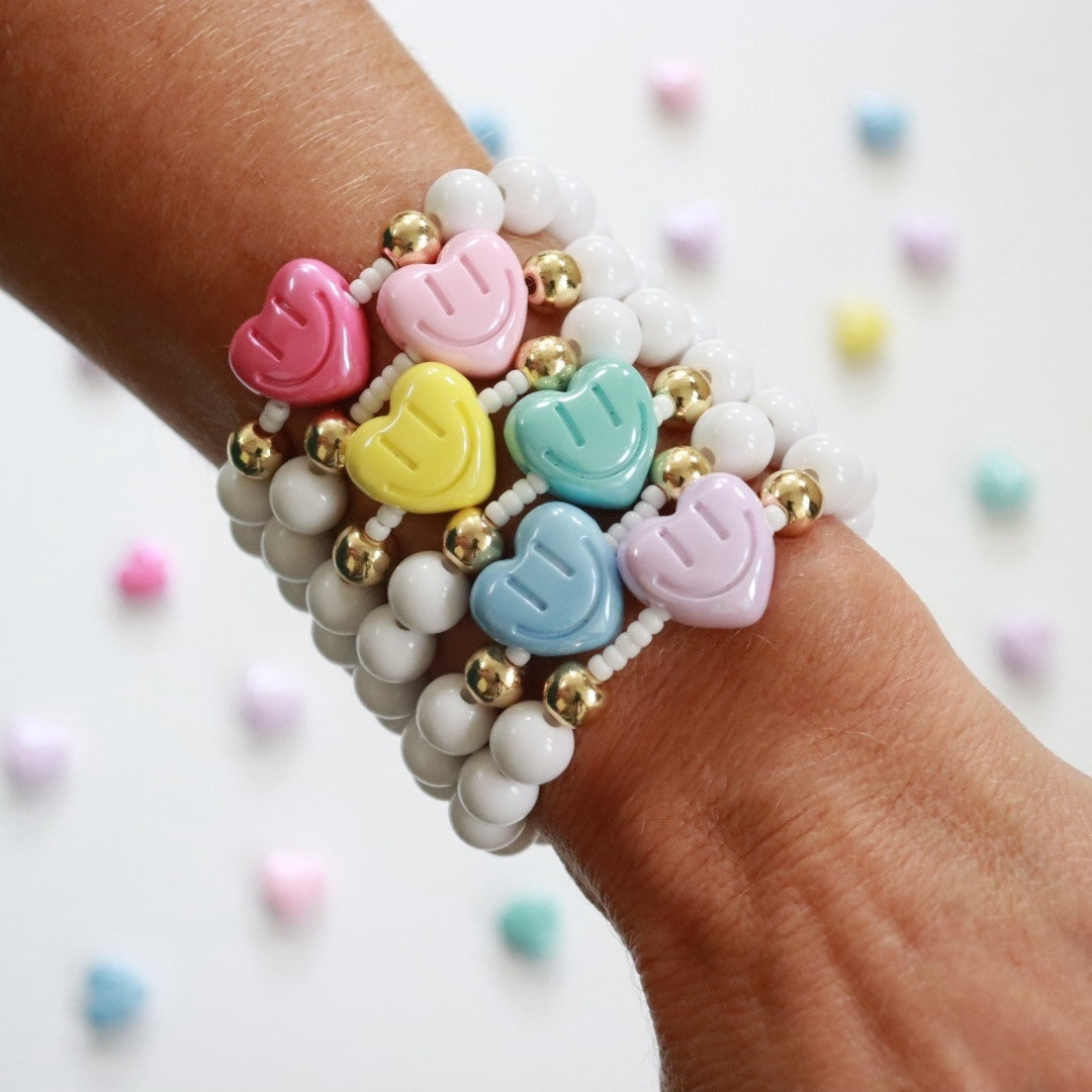 White beaded bracelet featuring a smiling heart bead in the centre strung over a row of Miyuki seed beads with gold plated spacer beads either side, creating a fidget element. The heart is available in 6 pretty colours. Handmade stretch fidget bracelet, the perfect gift for girls, teens & adults.