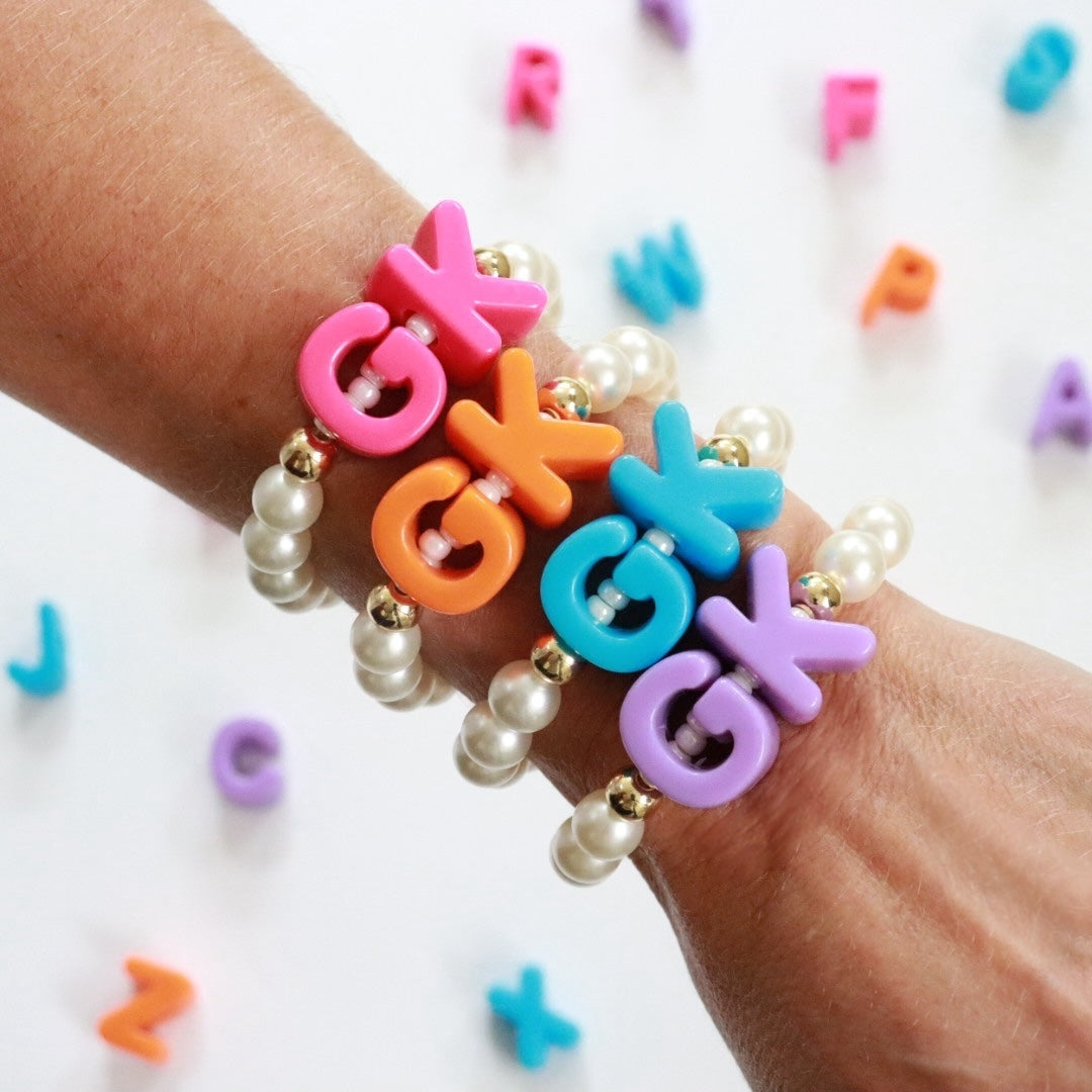 Pearl beaded bracelet featuring chunky colourful initials/letter beads in the centre strung over a row of pearl Miyuki seed beads with gold plated spacer beads either side. Handmade stretch bracelet, the perfect gift for girls, teens & adults.